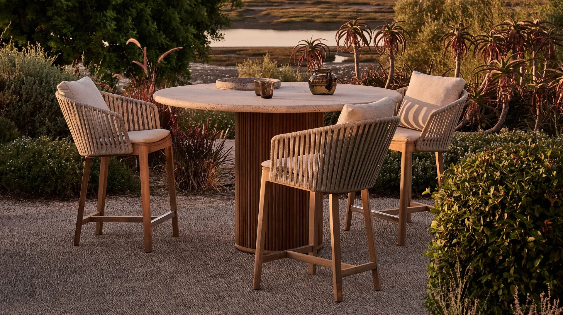 Tribù garden furniture on a terrace at dusk, teak lounge chairs around a low Tribù table woven in rope