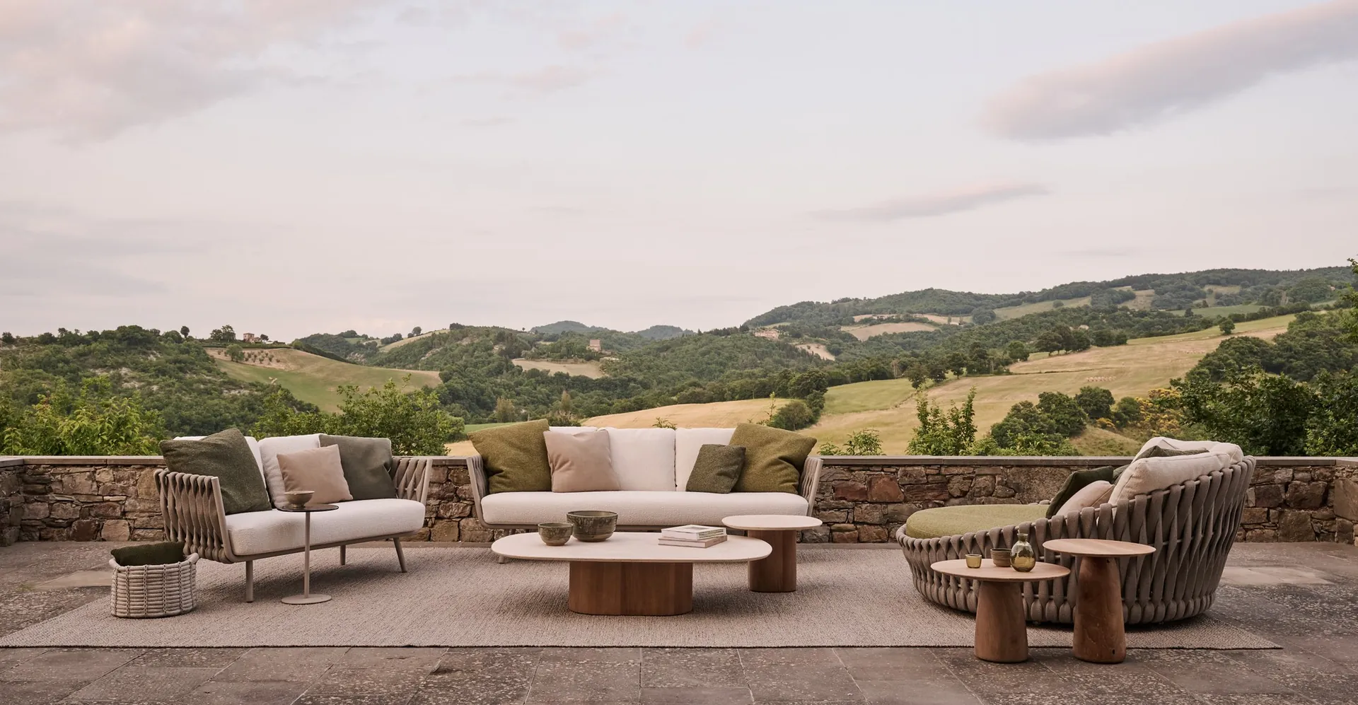 Tribù Tosca sofa, lounge chair and round braided daybed on a stone terrace above a valley