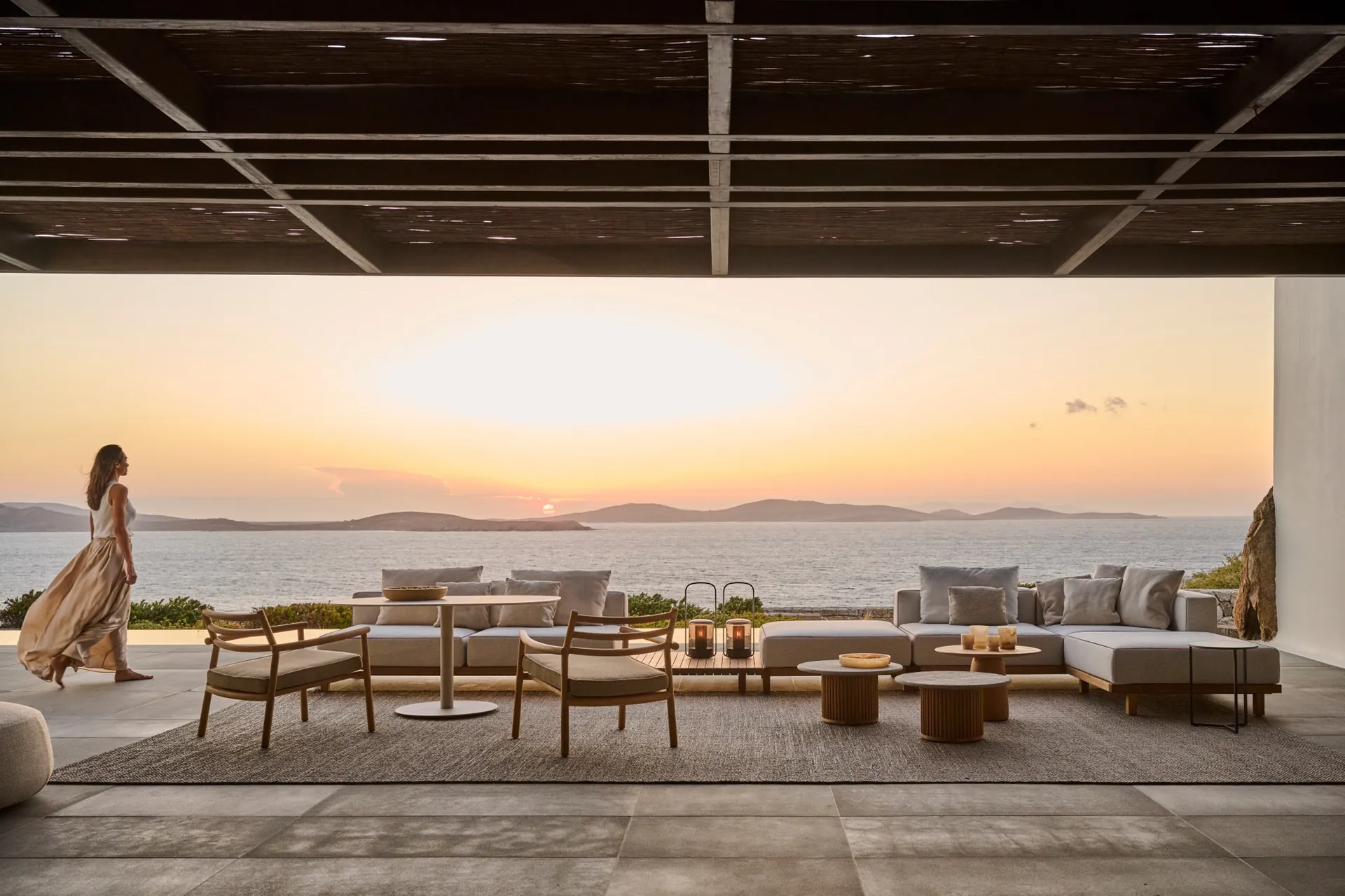 Tribù Ukiyo teak lounge chairs and a round dining table on a covered terrace above the sea